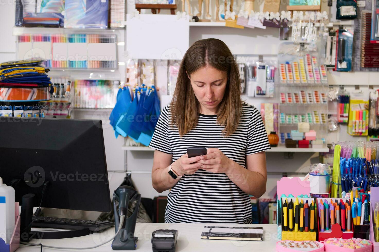 Young woman manager, seller in creative store, using mobile phone, standing at the counter and ordering stationery photo