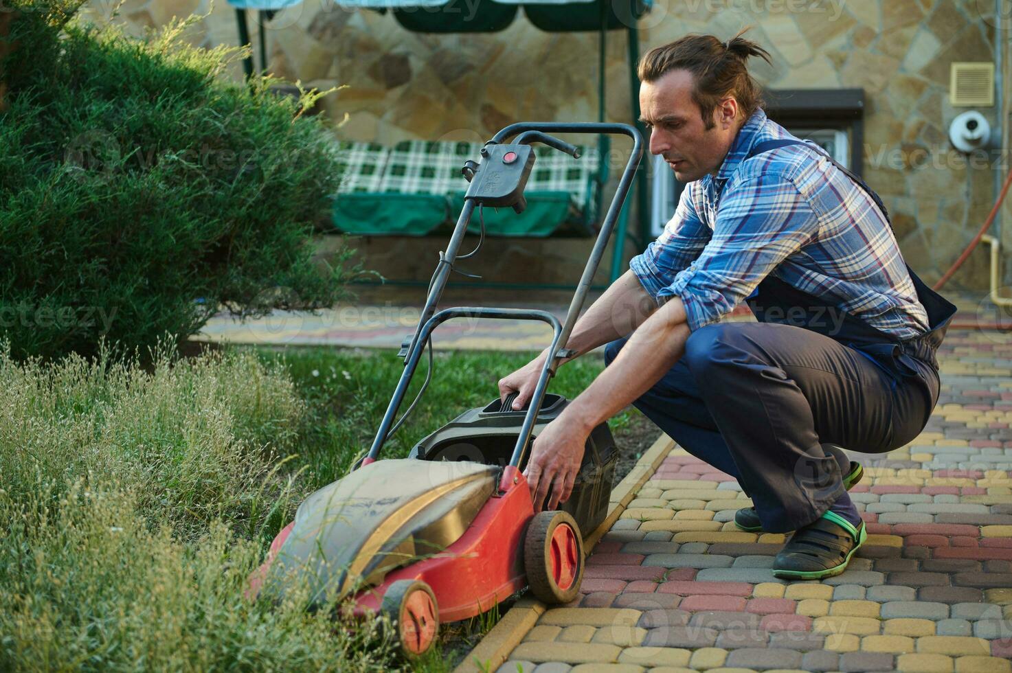 Professional gardener takes the cut grass out of the filter, recharges the electric lawn mower in the house backyard photo