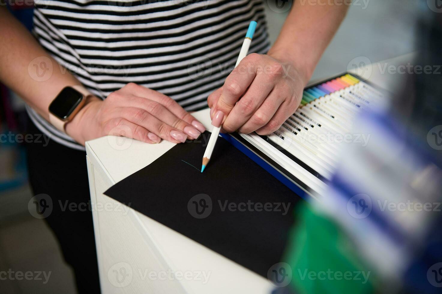 Close-up view of woman's hand testing color pencil, drawing on a black paper sheet. School stationery. Drawing supplies photo