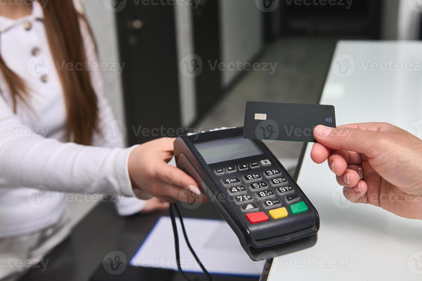 Close up manager at reception counter holding out POS terminal to client customer paying by credit card. NFC technology photo