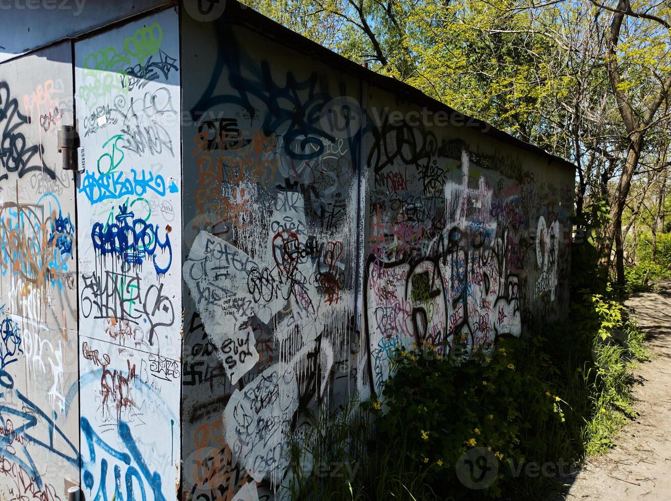 Abandoned old garage outlined by author's graffiti and overgrown with vegetation and moss. Ukraine, Zaporozhye, May 2023 photo