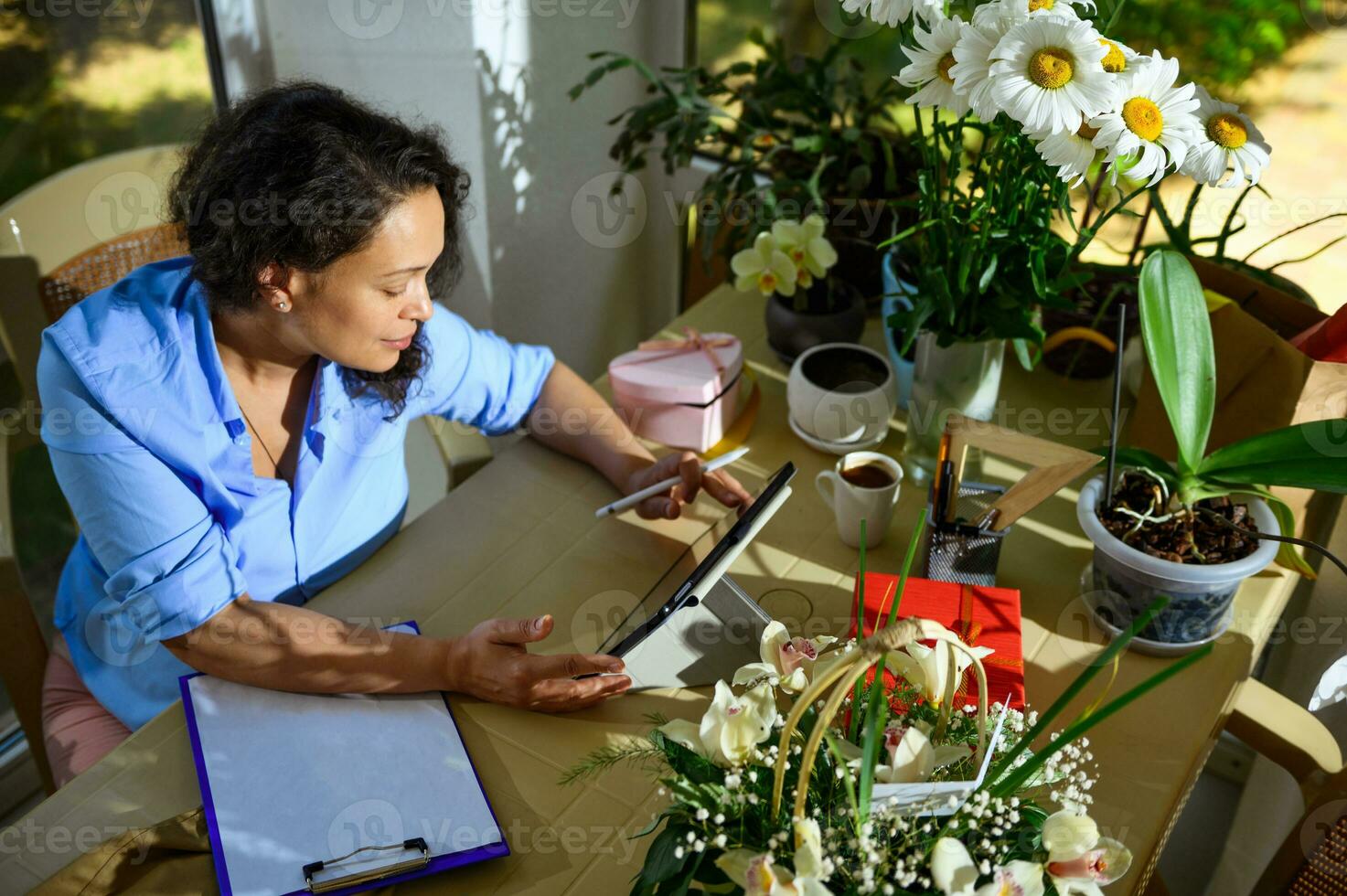 Beautiful multi-ethnic woman florist using a digital tablet, sketching, working on floral arrangement in flower shop photo