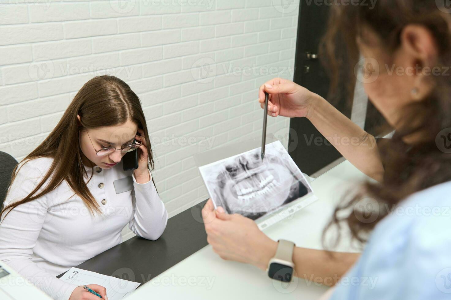 Female receptionist talks on mobile phone. Blurred foreground of a dentist holding dental x-ray panoramic radiography photo