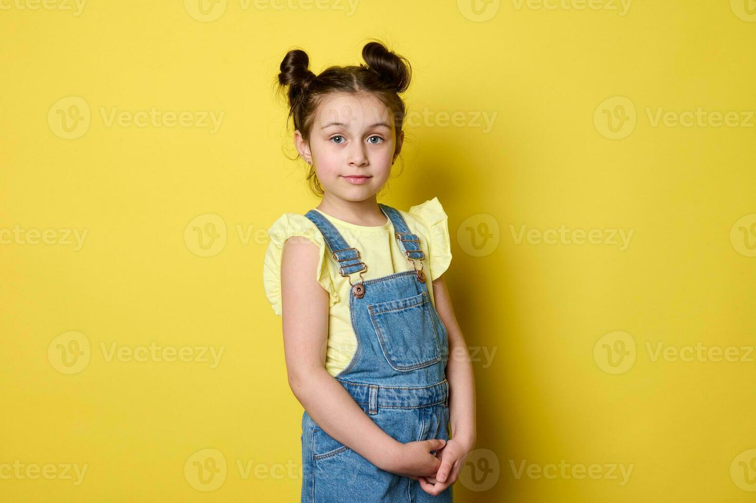 hermosa de moda pequeño niño niña con de moda peinado en casual azul mezclilla, mirando a cámara. contento infancia. foto