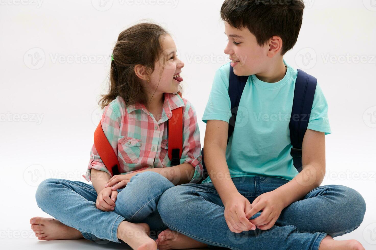 Adorable brother and sister, smart school kids with backpacks, smiling, making faces, showing tongue isolated on white photo