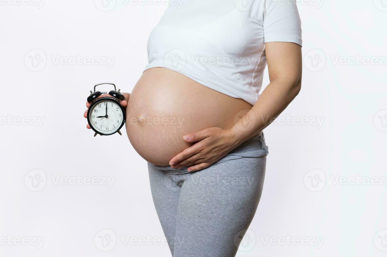 de cerca embarazada mujer con desnudo barriga sostiene alarma reloj. biológico reloj tictac. el embarazo. destinado a fecha de nacimiento. foto