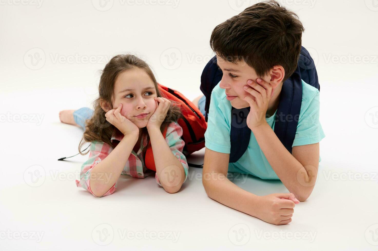 Happy smart school kids, a teen boy a little girl with backpacks talking together, isolated on white studio background photo