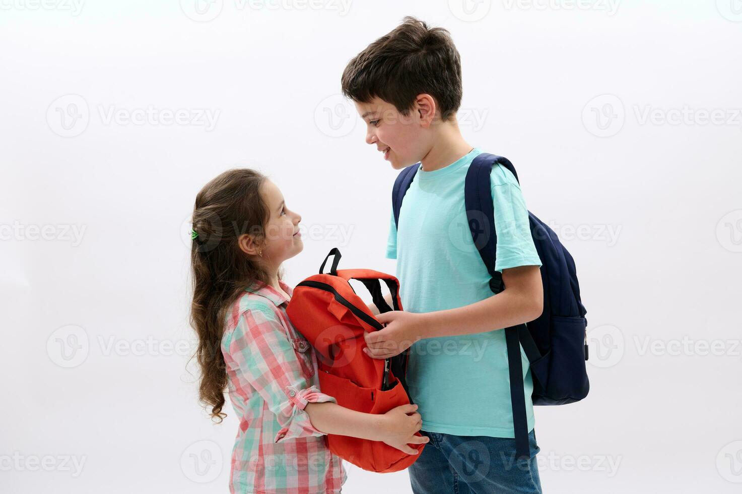 Happy children, preteen boy and girl with backpacks, smile looking at each other, isolated over white studio background photo