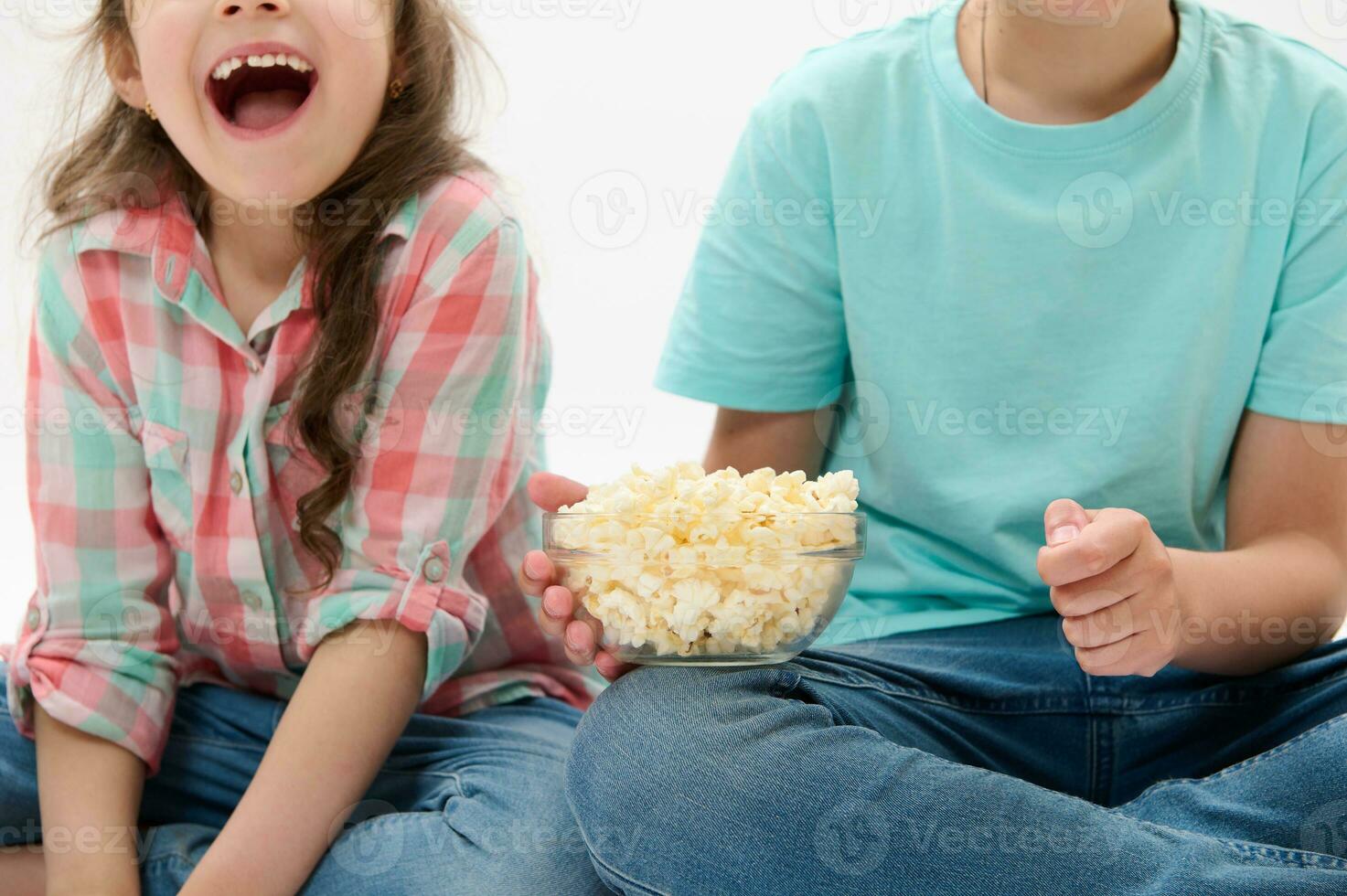 Details on a bowl of popcorn in the hands of cute children watching movies or cartoons over white isolated background photo