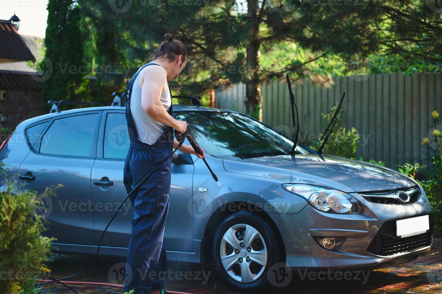 Full length portrait of a service man in blue work uniform, manually washing car with high pressure water jet outdoors. photo