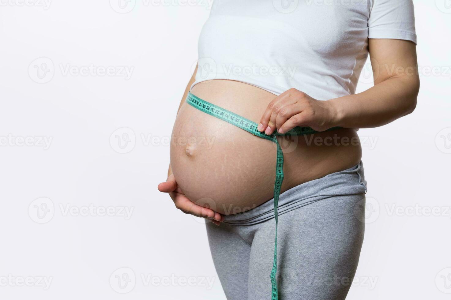 sección en medio de embarazada mujer medición su barriga con un cinta a mantener pista de su feto desarrollo, blanco antecedentes foto