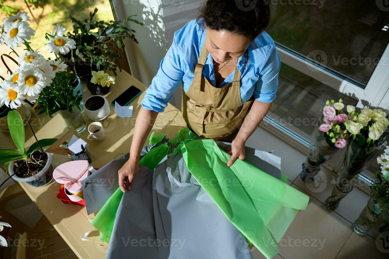 parte superior ver embarazada mujer floris laminación fuera envase papel mientras creando hermosa ramo de flores de flores en un floral Tienda foto