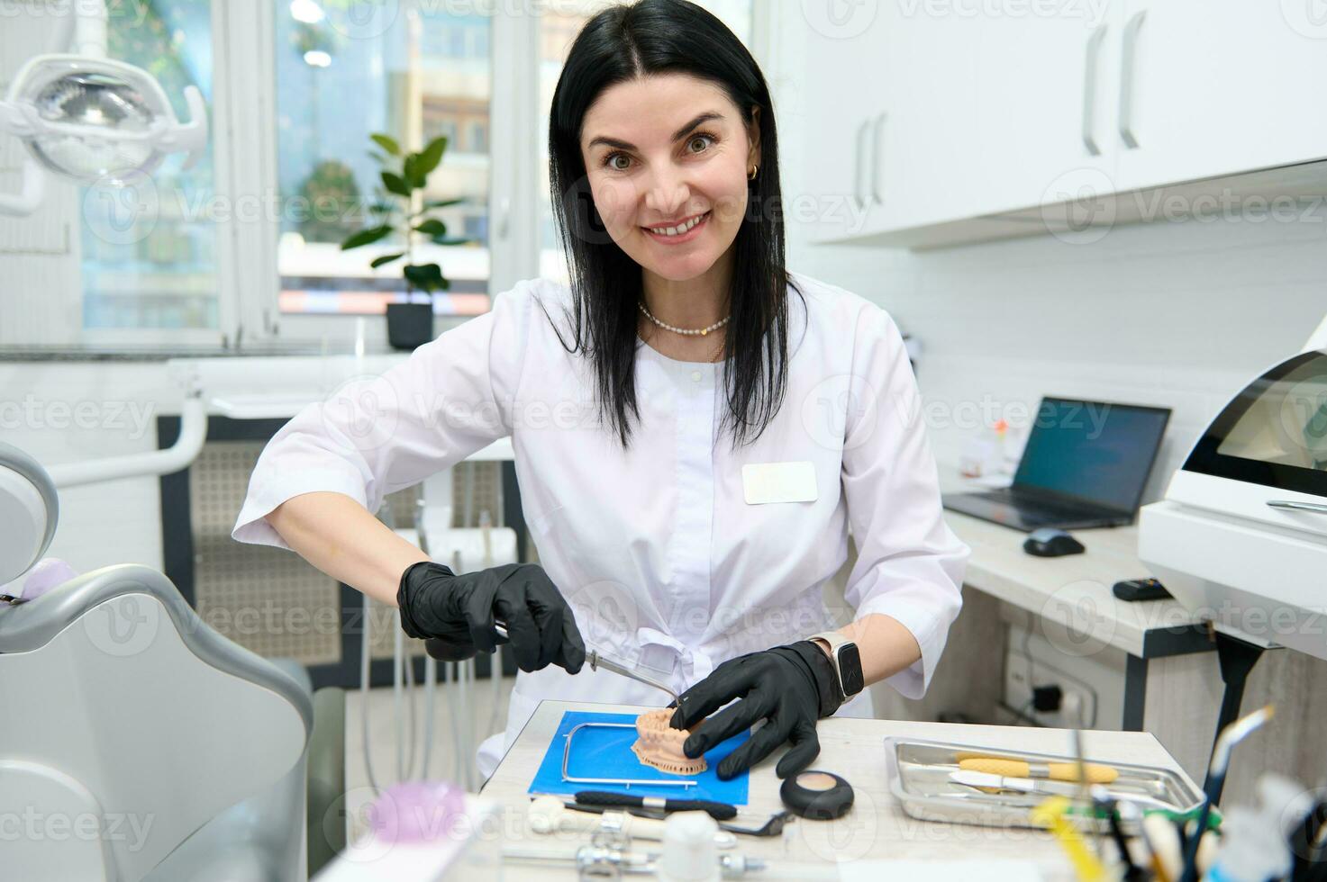 Experienced smiling woman prosthetic engineer, dental technician works with plaster mold cast of human jaw. Orthodontics photo