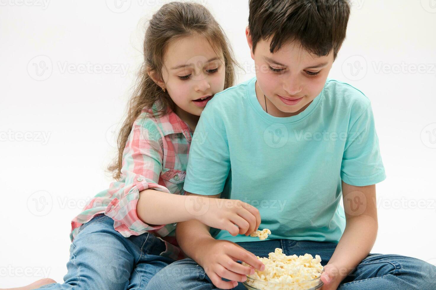 Close-up lovely children kids - preteen boy and cute baby girl eating popcorn, isolated over white studio background photo