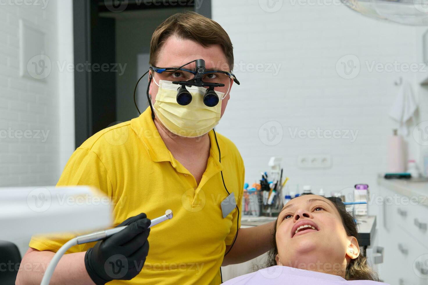 dentista en ortodoncista prismáticos, sostiene dental perforar, realiza dientes tratamiento a embarazada paciente en odontología clínica foto