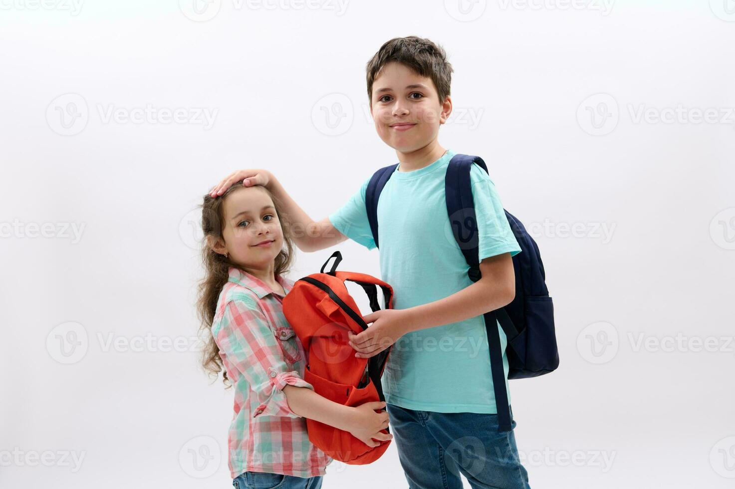 Handsome teen boy with backpack, strokes his younger sister, ready to go at school, start new semester of academic year photo