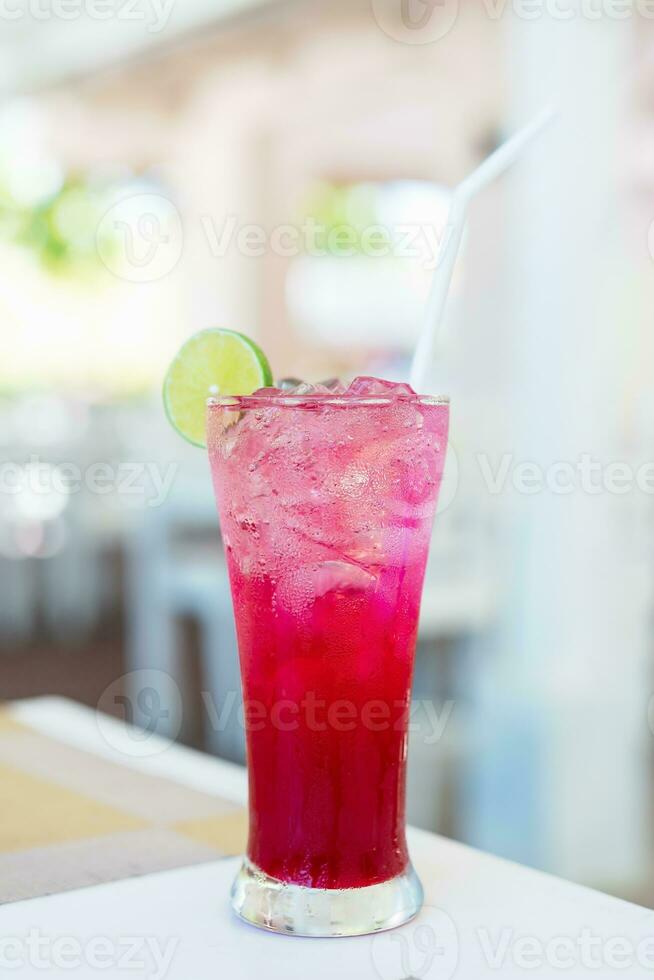 Cold red Juice with iced cub and a slice of lemon on top of glass on table at restaurant. Glass of alcoholic refreshing drink decorated lemon slice. Beach bar, summer sea resort concept. photo