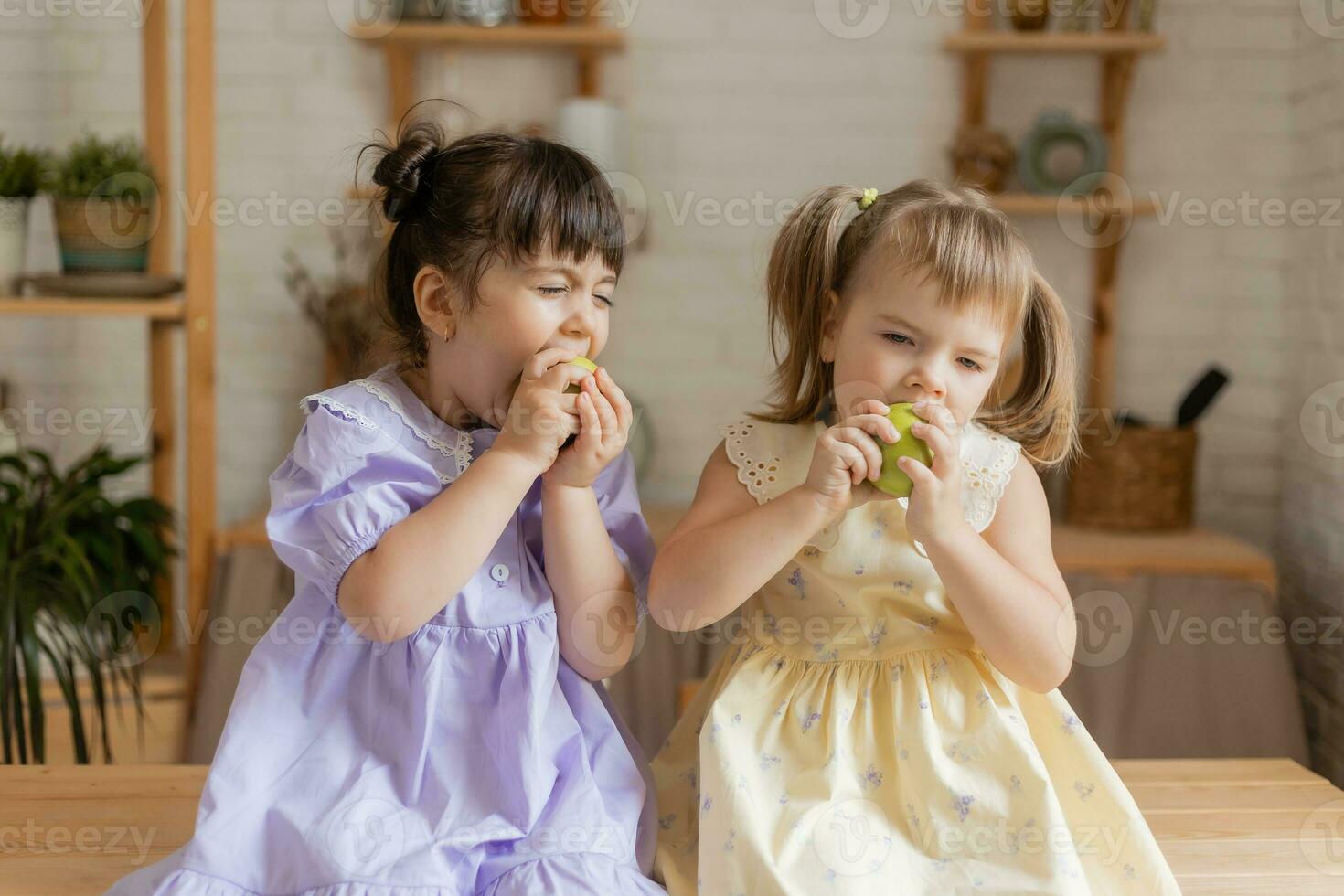 pequeño contento muchachas tonto alrededor en el cocina y comer manzanas foto