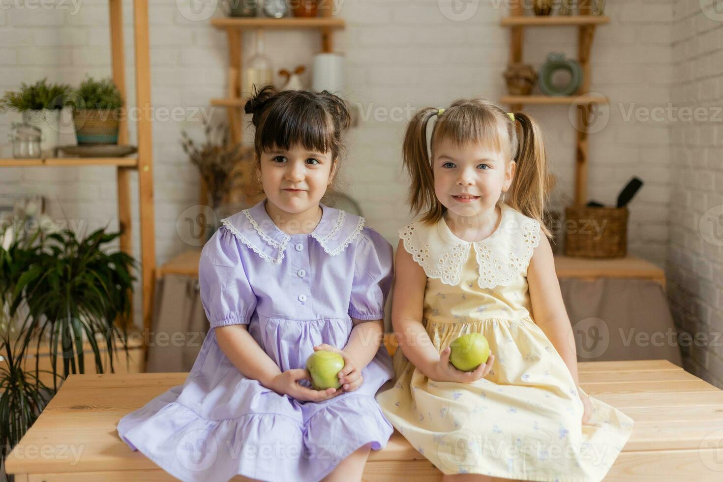 pequeño contento muchachas tonto alrededor en el cocina y comer manzanas foto