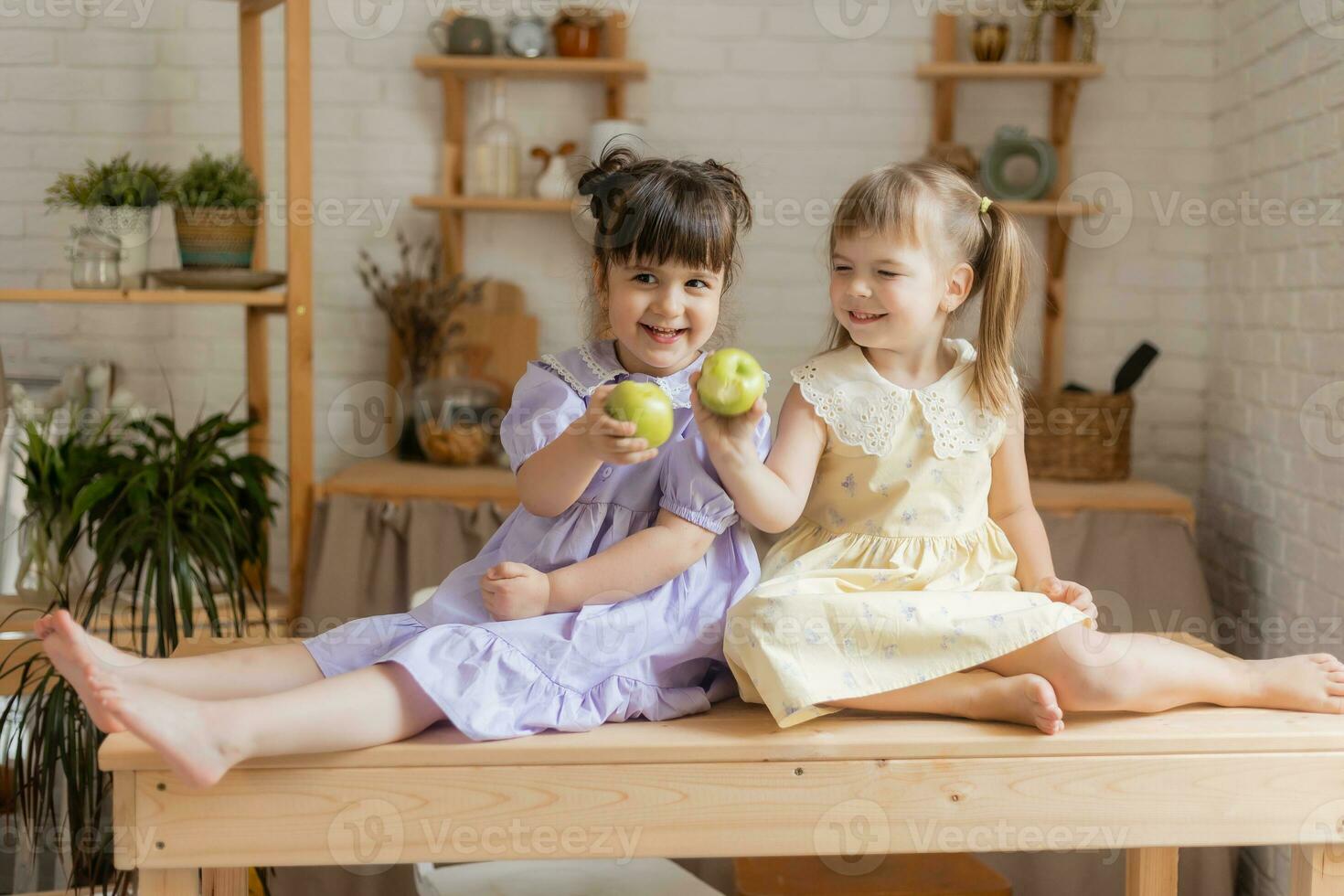 pequeño contento muchachas tonto alrededor en el cocina y comer manzanas foto