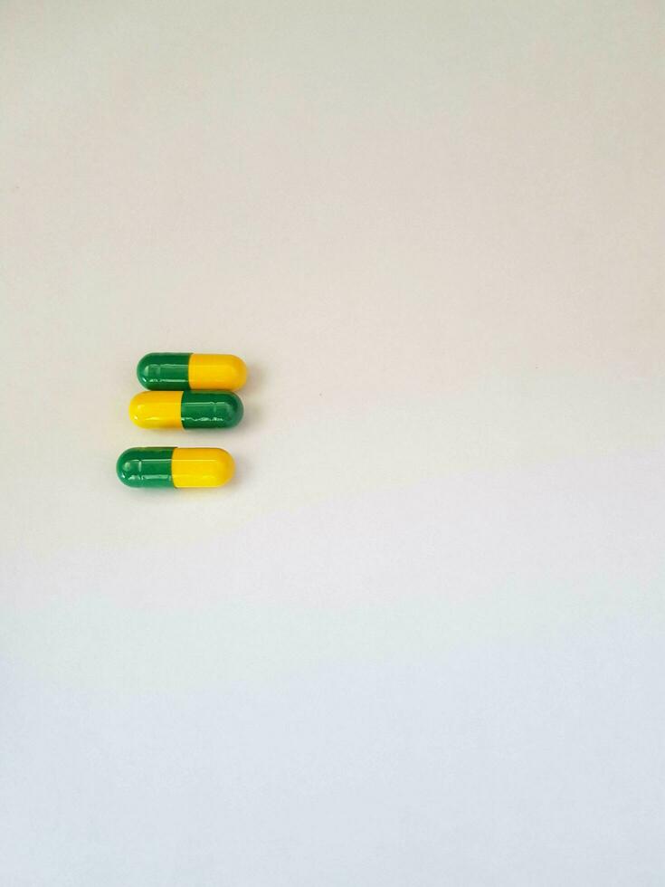 Isolated white photo of three medicine capsules green and yellow.