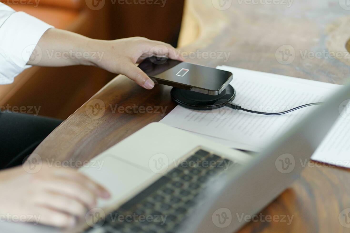 Charging mobile phone battery with wireless charging device in the table. Smartphone charging on a charging pad. Mobile phone near wireless charger Modern lifestyle technology concept photo