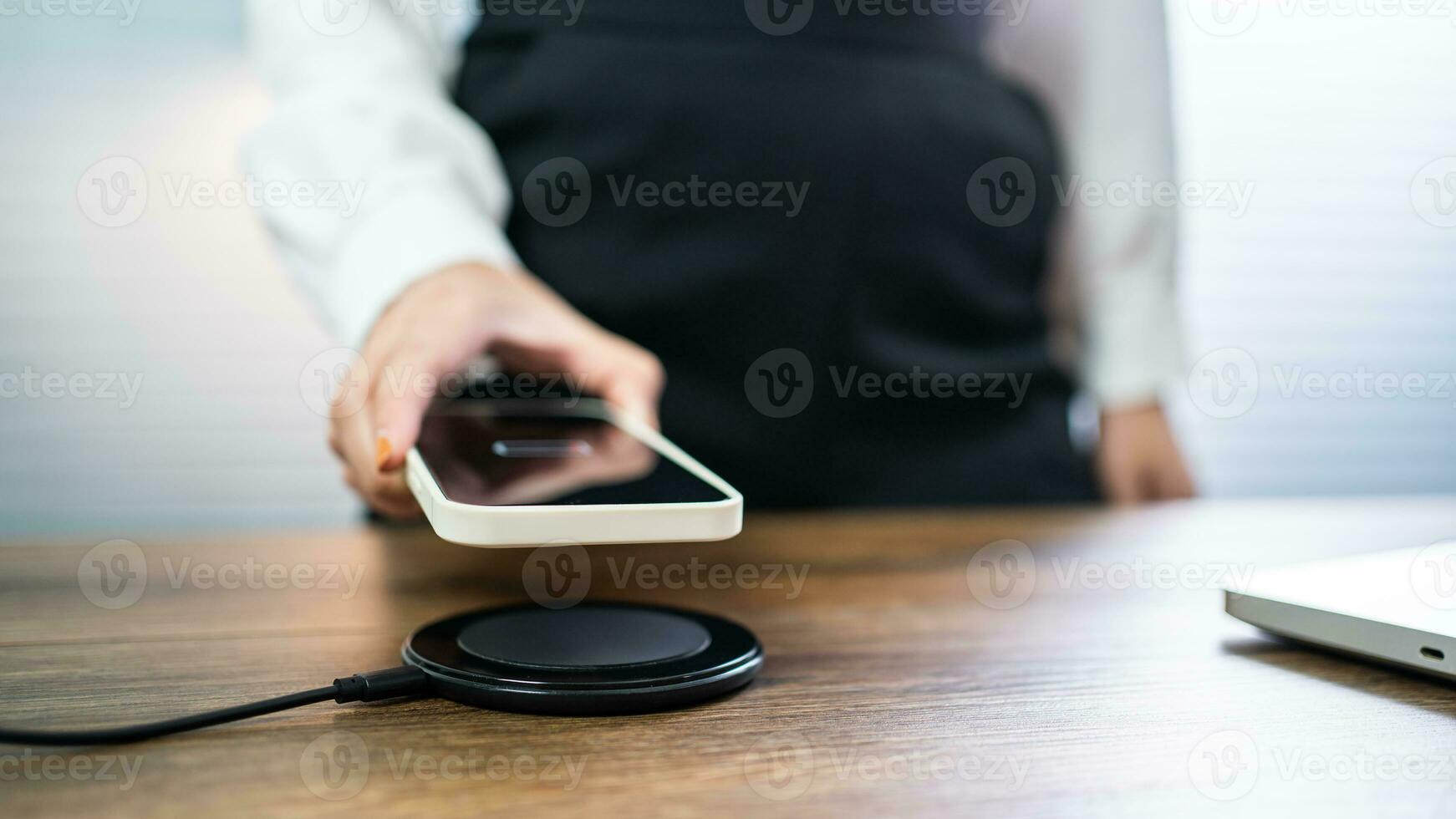 Charging mobile phone battery with wireless charging device in the table. Smartphone charging on a charging pad. Mobile phone near wireless charger Modern lifestyle technology concept. photo