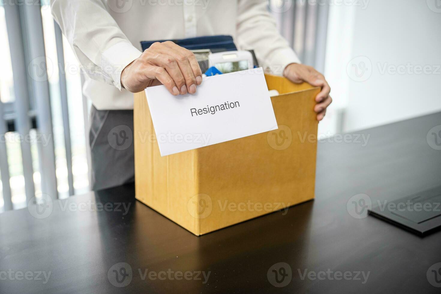 Business man sending resignation letter and packing Stuff Resign Depress or carrying business cardboard box by desk in office. Change of job or fired from company photo