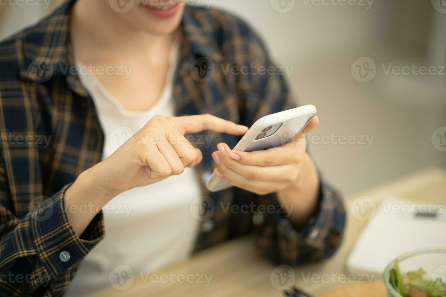 contento hermosa asiático mujer con teléfono comiendo Fresco ensalada a mesa en cocina y utilizando solicitud mensajes de texto en teléfono inteligente mientras comiendo sano comida foto