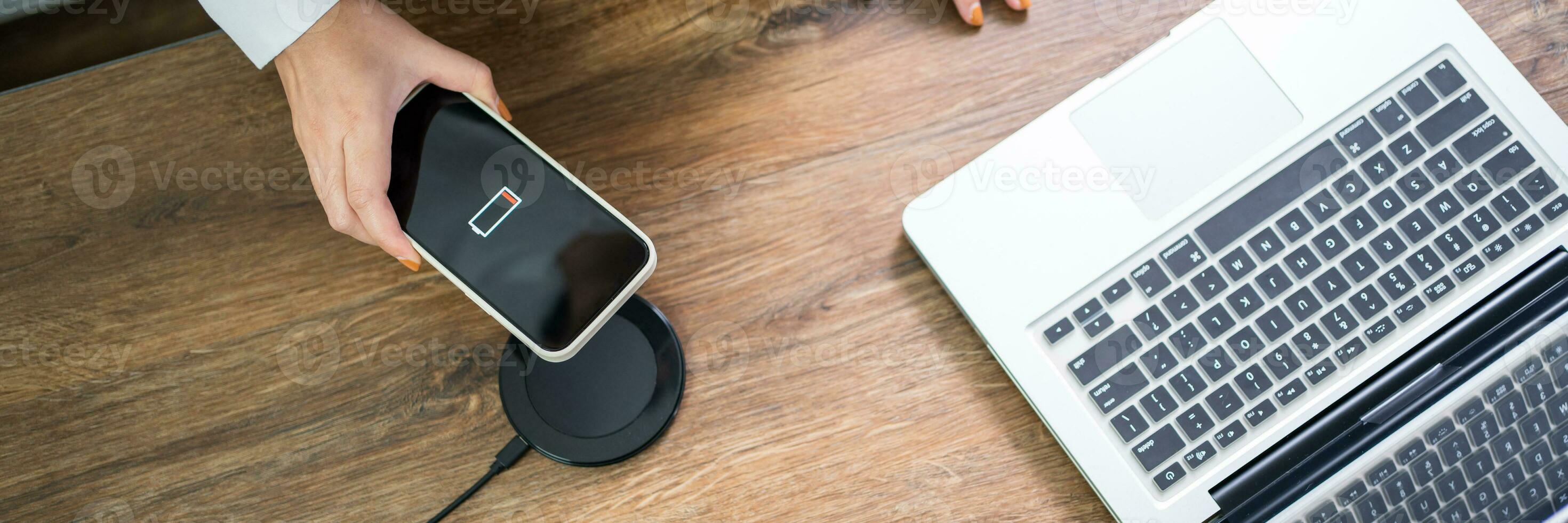 Charging mobile phone battery with wireless charging device in the table. Smartphone charging on a charging pad. Mobile phone near wireless charger Modern lifestyle technology concept. photo