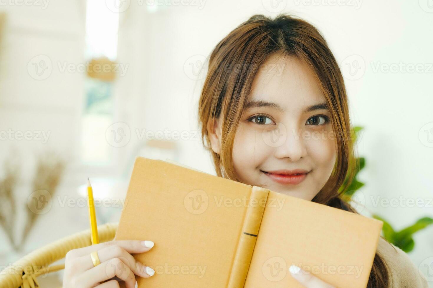 Portrait of a young female student covers her face with a yellow book photo