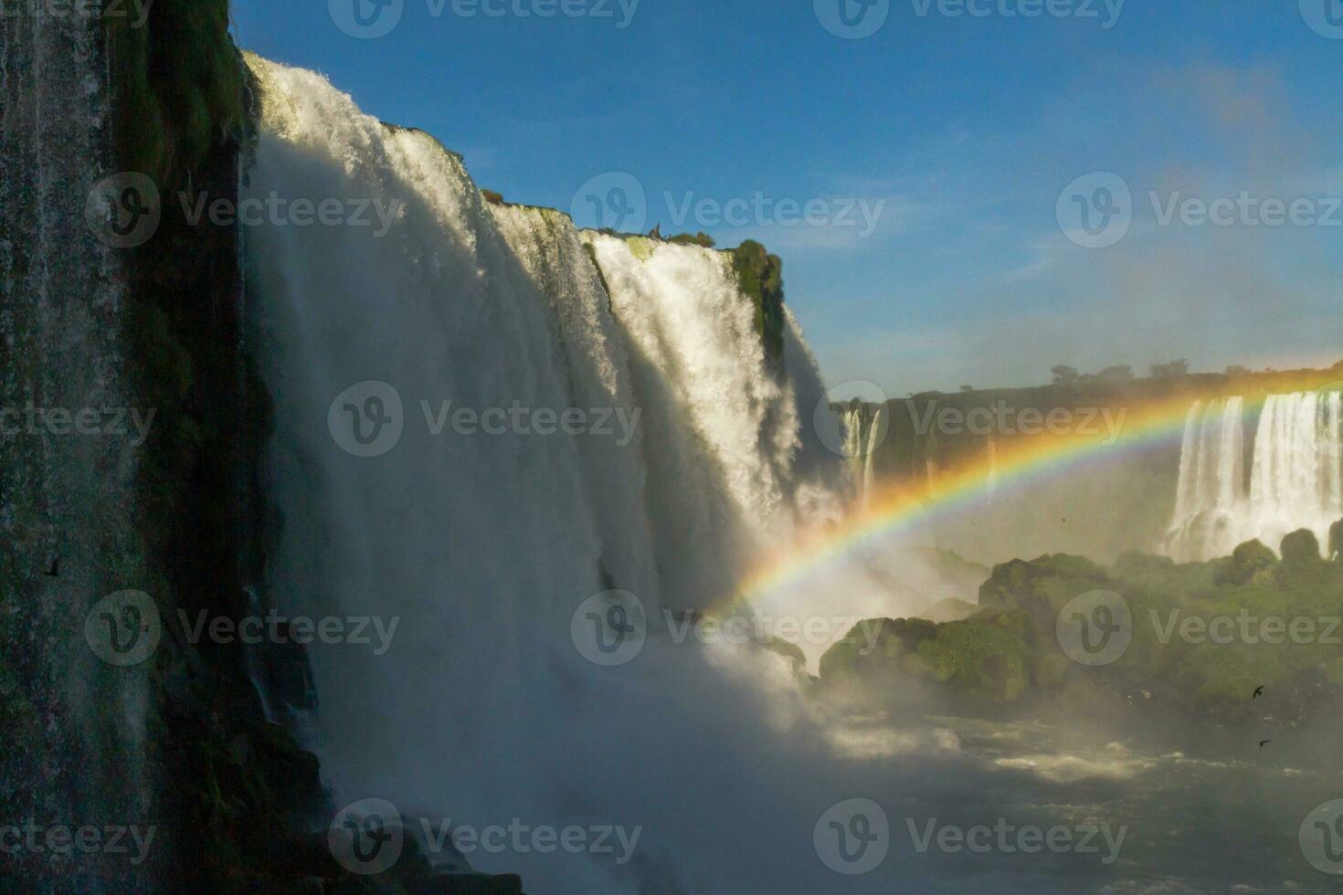 Iguazu Falls on the border between Argentina and Brazil with beautiful rainbows and lots of vegetation and lots of water falling down them photo