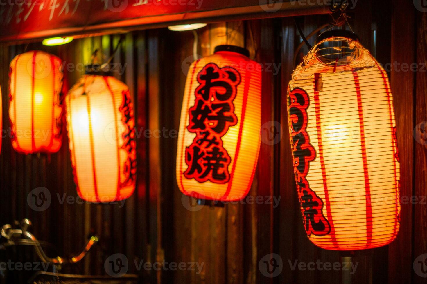 Red Japanese lanterns with inscriptions of Okonomiyaki which is a traditional food, on the door of a restaurant where it is cooked photo