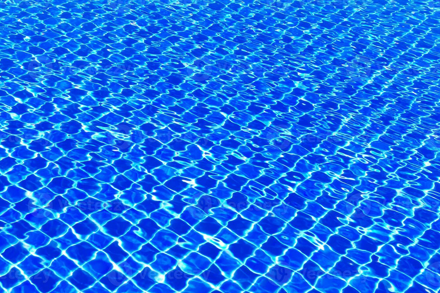 The blue tiles floor under the clear water in the swimming pool background, Swimming pool surface with floor mosaic tiles in blue photo