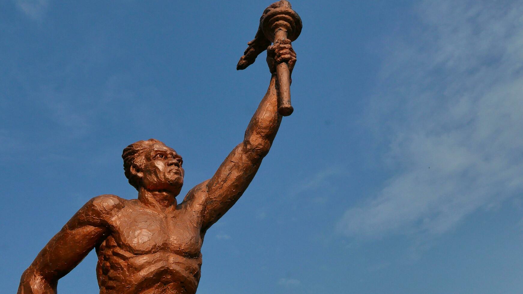 Surakarta, Indonesia, 20th June 2023, Statue of spirit of sport in a form of man holding torch against blue sky, Patung obor manahan located at the Manahan stadium Surakarta photo