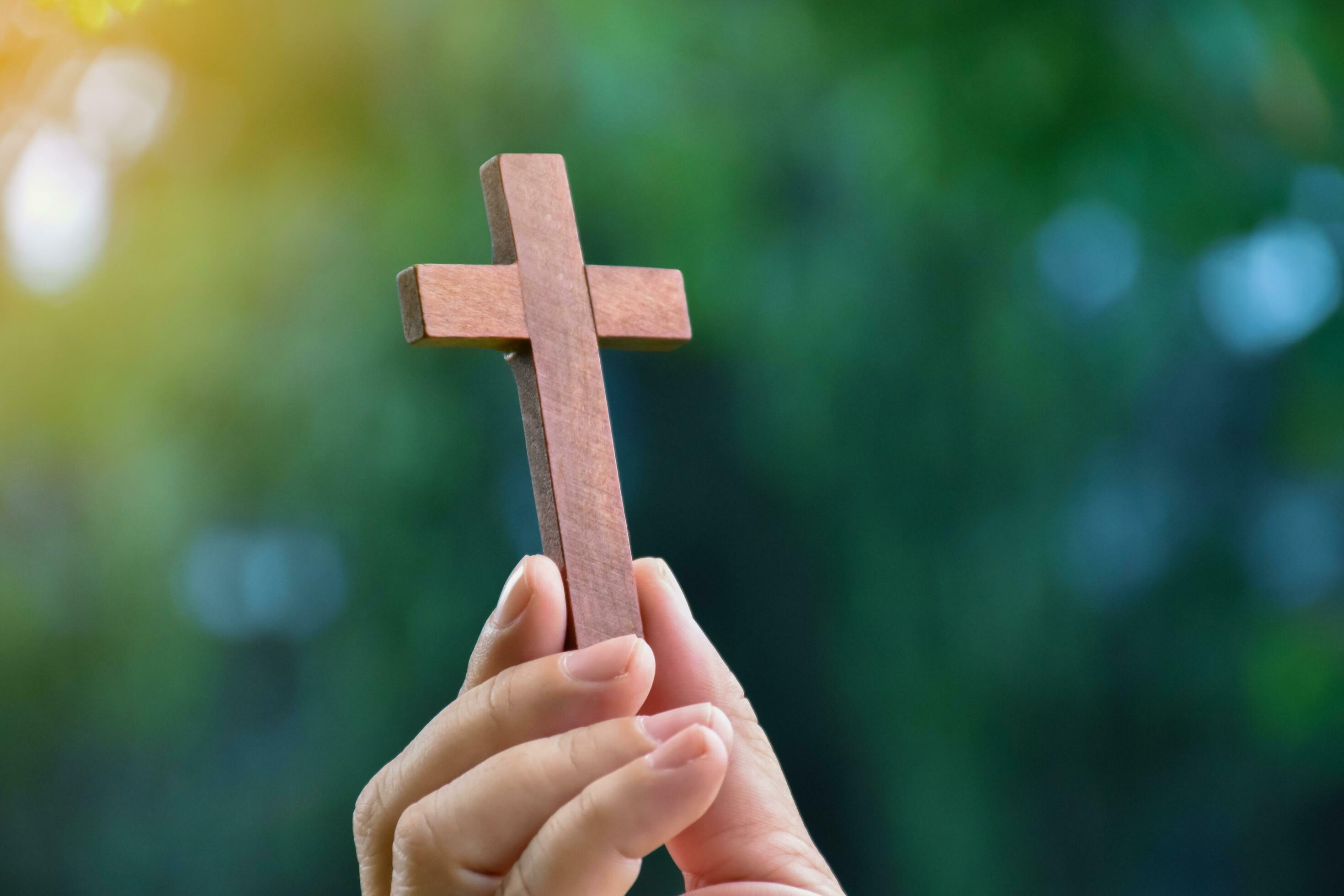 Wooden cross holding in hand with green and fresh forest background