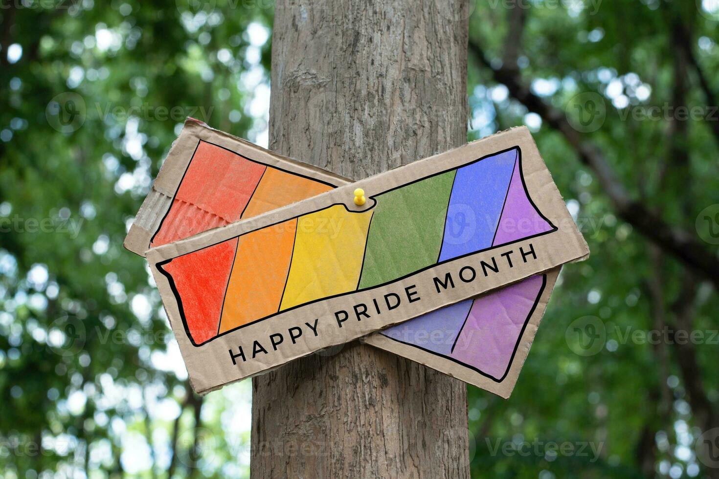 Signpost which has rainbow drawing with texts 'Happy Pride Month' sticked on tree trunk in public park to celebrate and to greet LGBT people events in pride month and to respect gender diversity. photo