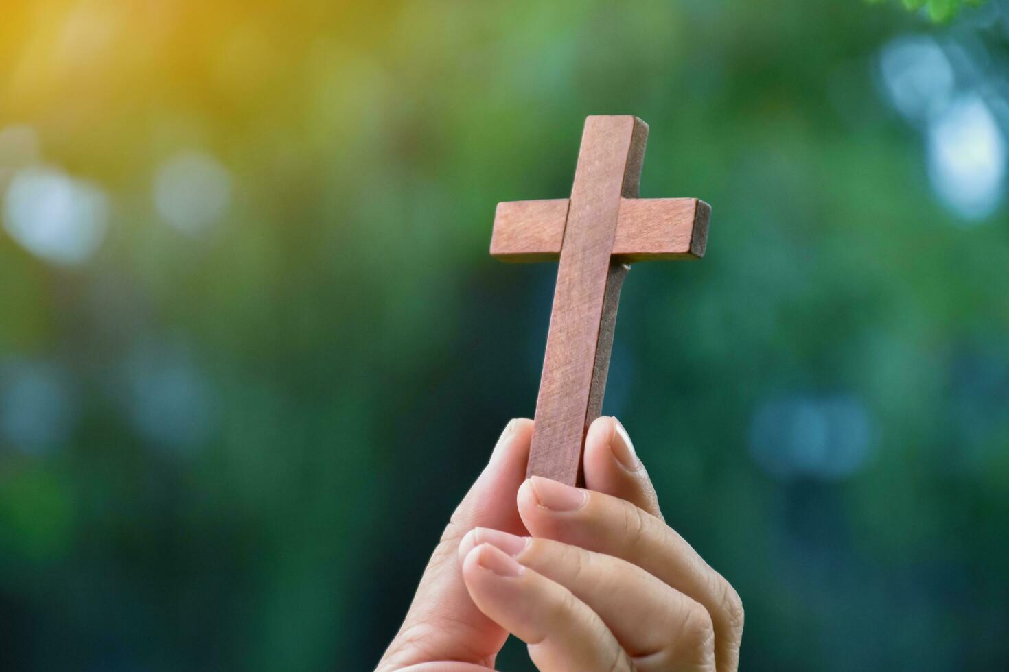 Wooden cross holding in hand with green and fresh forest background, concept for love of god in people around the world. photo