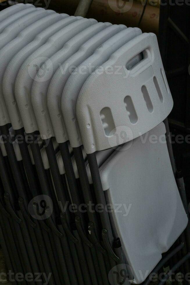 Plastic folding chairs are white stacked on top photo