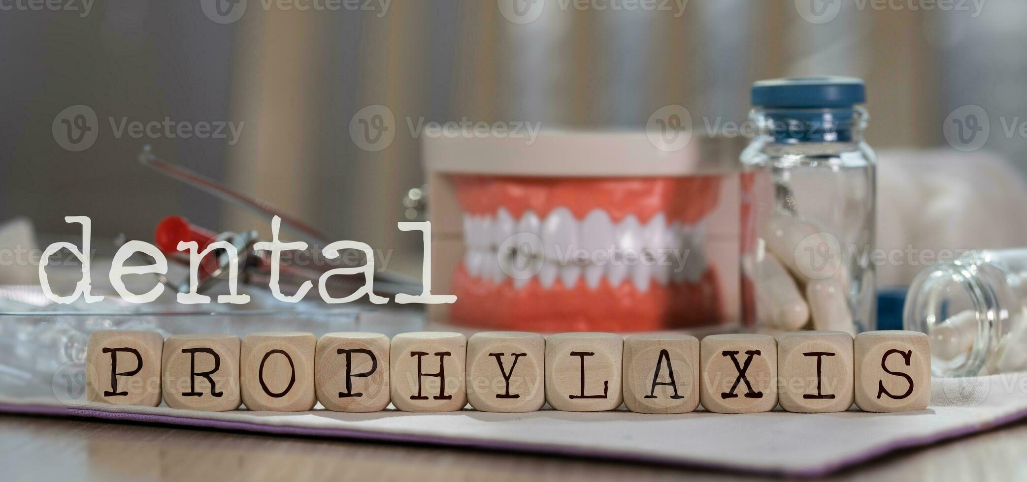 Words DENTAL PROPHYLAXIS composed of wooden dices. Pills, documents, pen, human jaw model in the background. photo