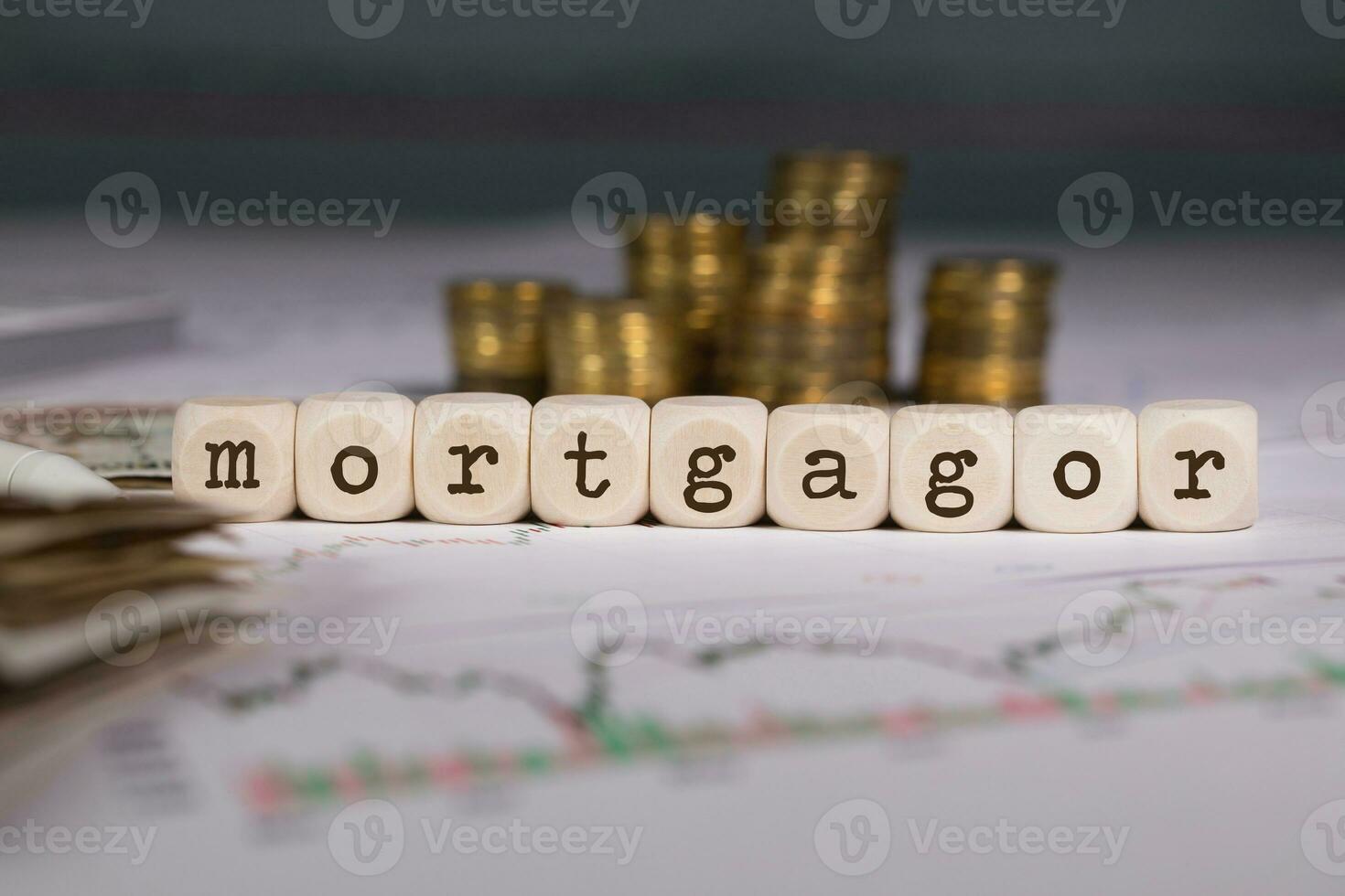 Word MORTGAGOR composed of wooden letter. Stacks of coins in the background. photo