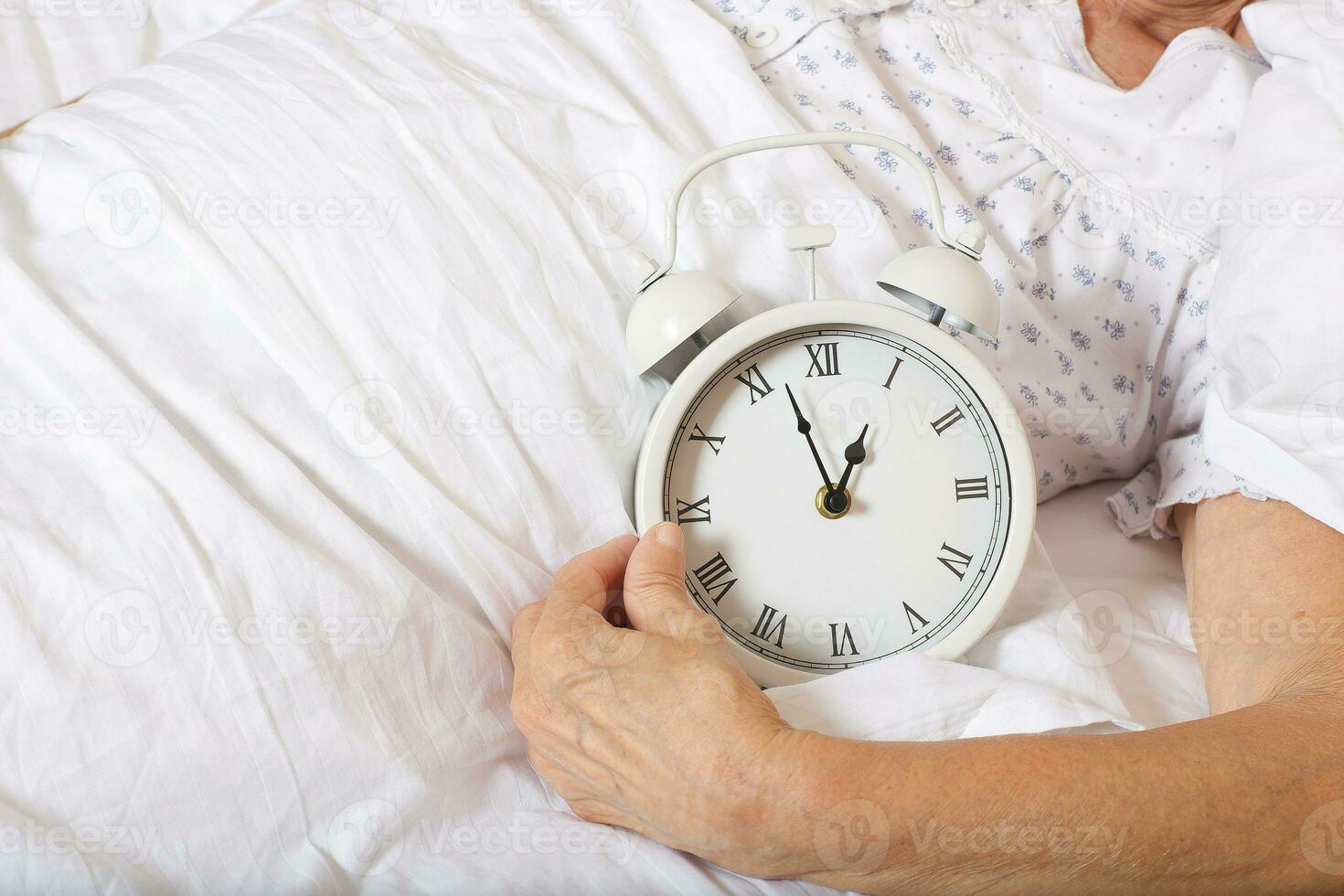 Vintage alarm clock on the bed of senior woman photo