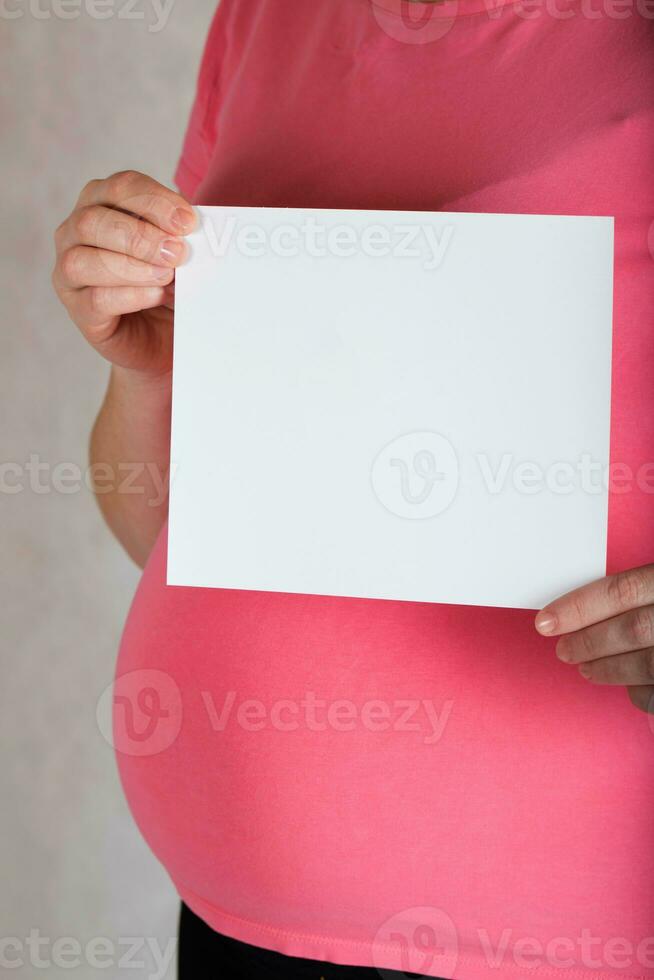 Young pregnant between 30 and 35 years old woman keeps a  blank white sheet of paper. photo