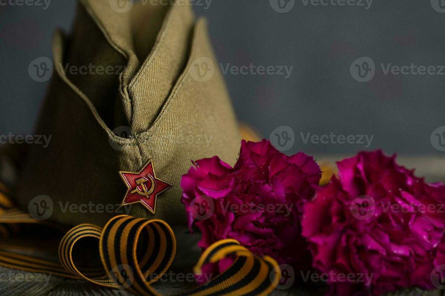 Military cap, carnations, Saint George ribbon on a wooden surface. photo