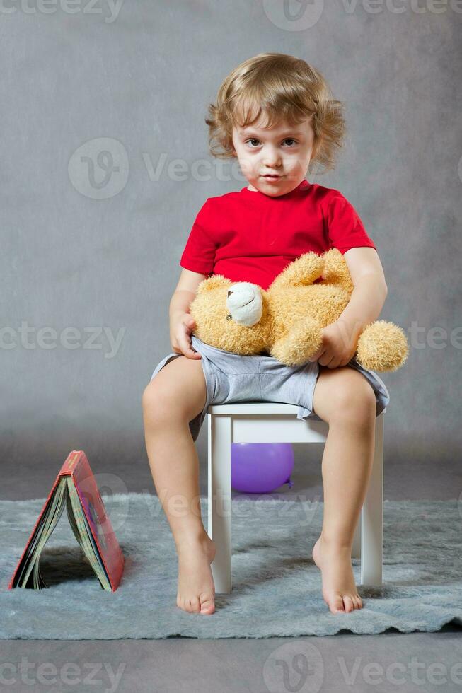 A boy of three years old sits on a white chair. photo