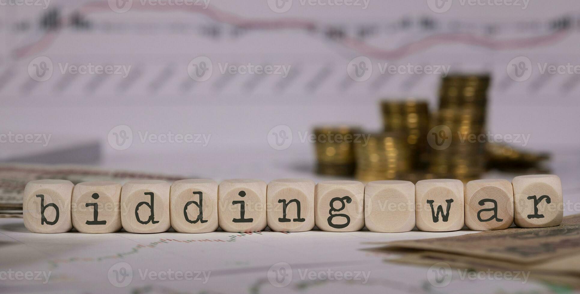 Words BIDDING WAR composed of wooden letter. Stacks of coins in the background. photo