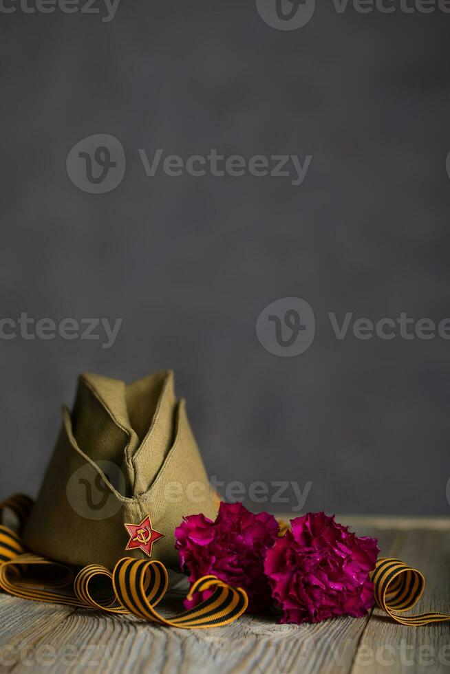 Military cap, carnations, Saint George ribbon on a wooden surface. photo