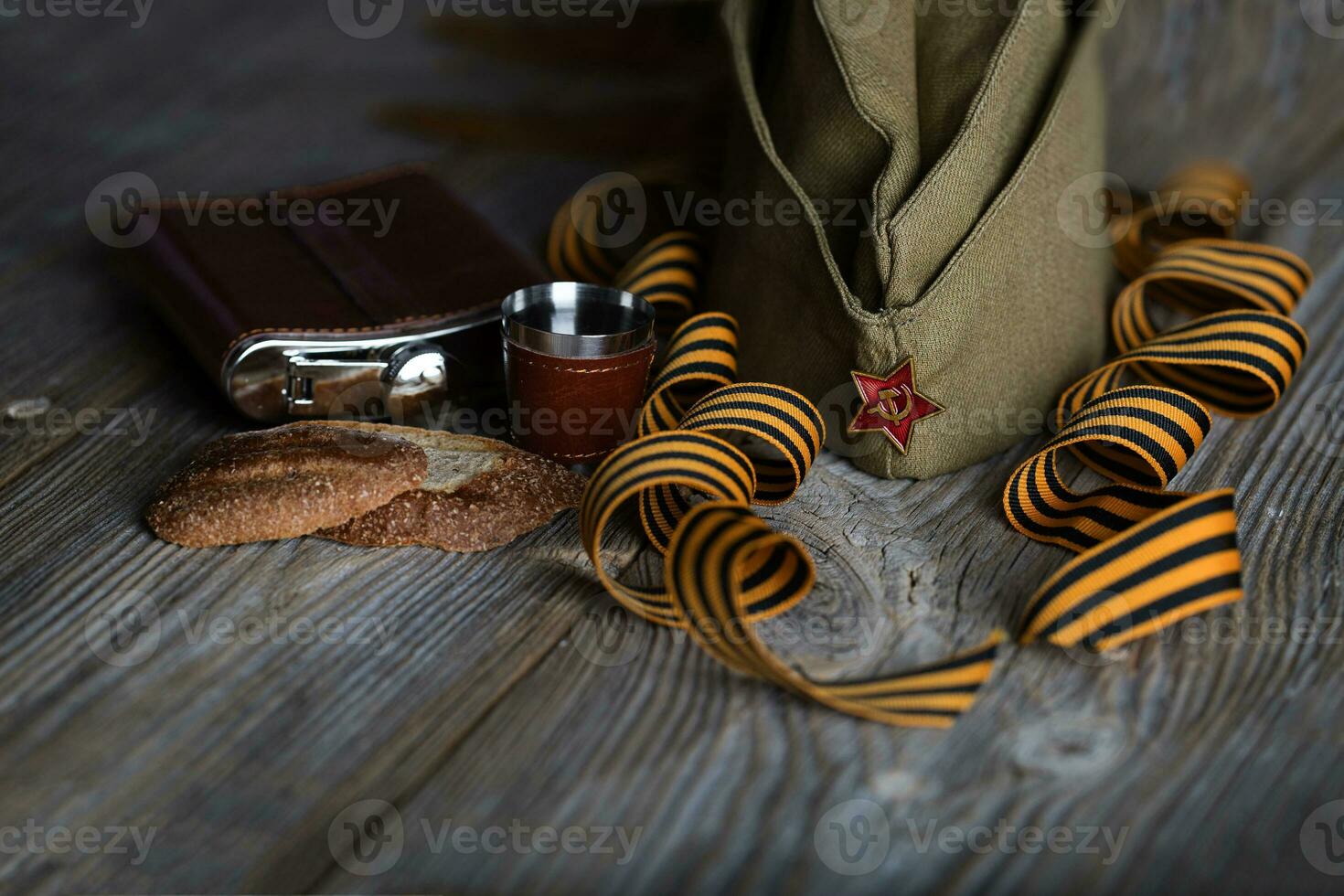 Military cap, carnations, Saint George ribbons, flask with alcohol  on a wooden surface. photo