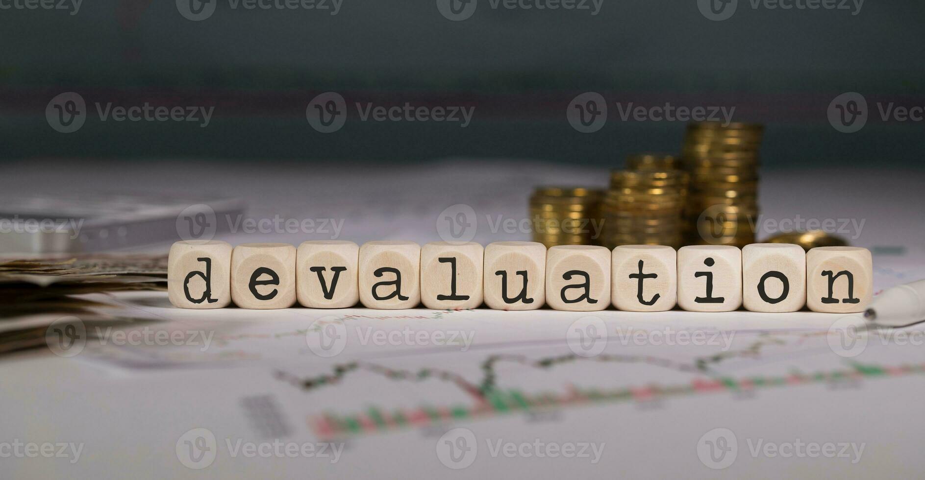 Word DEVALUATION composed of wooden letter. Stacks of coins in the background. photo