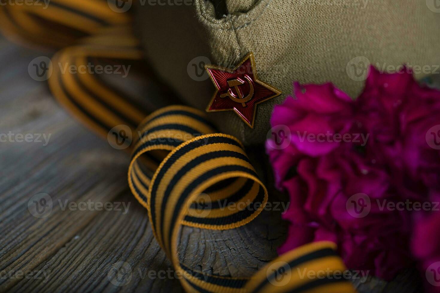 Military cap, carnations, Saint George ribbon on a wooden surface. photo